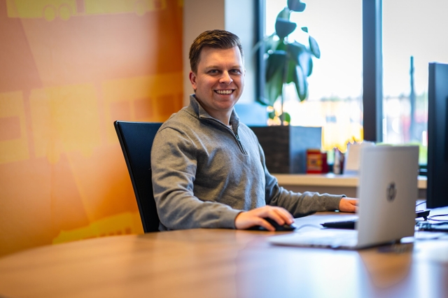 Een kantoormedewerker zit achter zijn laptop en glimlacht